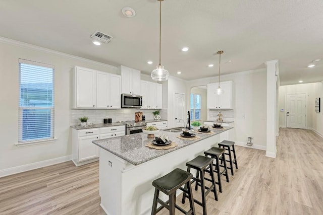 7517 Knockfin Dr, Austin, TX 78744 - kitchen with appliances with stainless steel finishes, ornamental molding, light wood-style flooring, a center island with sink, and a breakfast bar area