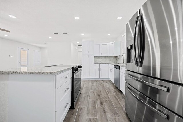 605 W Washington Ave, Copperas Cove, TX 76522 - kitchen featuring appliances with stainless steel finishes, light stone counters, white cabinets, decorative backsplash, and light wood finished floors