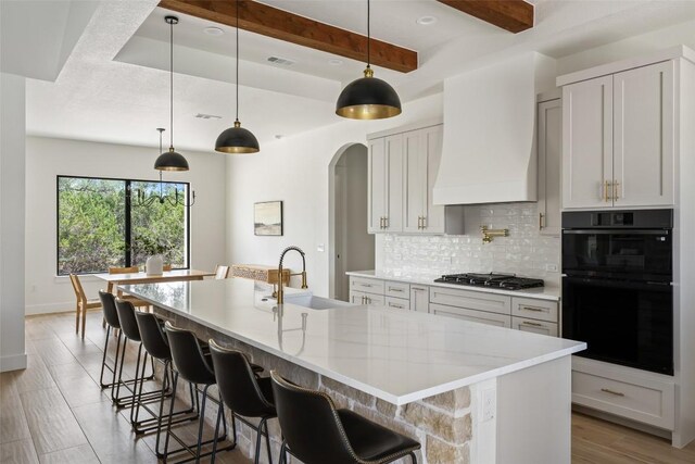1129 Madrone Rd, Fischer, TX 78623 - kitchen featuring stainless steel gas cooktop, decorative backsplash, arched walkways, a large island, and custom exhaust hood