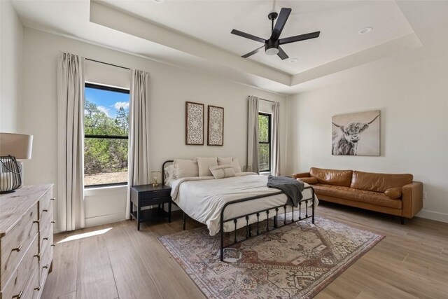 1129 Madrone Rd, Fischer, TX 78623 - bedroom featuring a tray ceiling, multiple windows, light wood-style flooring, and a ceiling fan