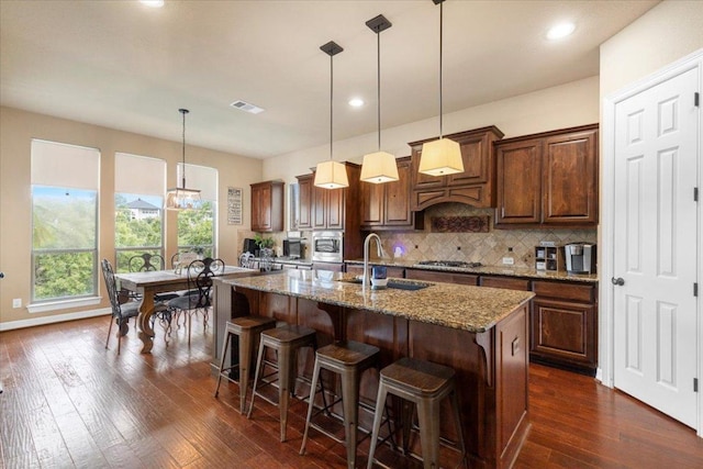 2308 First Vw, Leander, TX 78641 - kitchen featuring tasteful backsplash, light stone counters, dark wood-style floors, a kitchen island with sink, and stainless steel gas stovetop