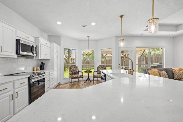 103 El Norte Ct, Lakeway, TX 78734 - kitchen featuring stainless steel appliances, tasteful backsplash, light stone countertops, white cabinets, and hanging light fixtures