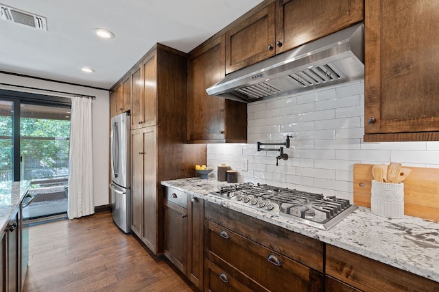 2717 Jorwoods Dr, Austin, TX 78745 - kitchen with exhaust hood, stainless steel appliances, decorative backsplash, dark wood-type flooring, and light stone counters