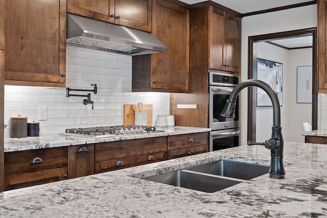 2717 Jorwoods Dr, Austin, TX 78745 - kitchen with under cabinet range hood, stainless steel appliances, decorative backsplash, light stone countertops, and crown molding