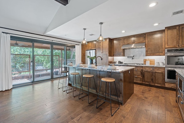 2717 Jorwoods Dr, Austin, TX 78745 - kitchen with stainless steel appliances, under cabinet range hood, decorative backsplash, light stone countertops, and dark wood-type flooring