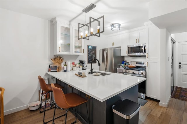 3431 N Hills Dr Unit 112, Austin, TX 78731 - kitchen with stainless steel appliances, a kitchen bar, glass insert cabinets, a peninsula, and light wood-style floors