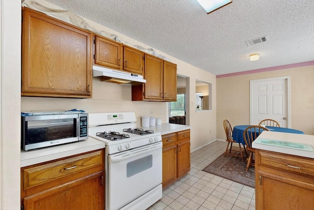 12062 Lincolnshire Dr, Austin, TX 78758 - kitchen featuring white range with gas cooktop, under cabinet range hood, stainless steel microwave, brown cabinetry, and light countertops