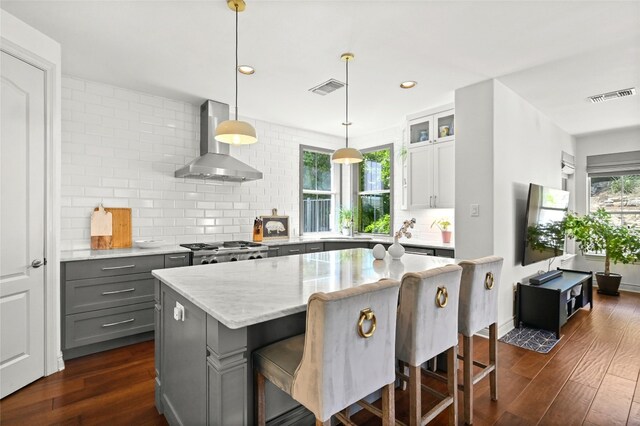 4332 Canoas Dr, Austin, TX 78730 - kitchen with wall chimney exhaust hood, backsplash, dark wood-style flooring, light stone countertops, and a kitchen bar