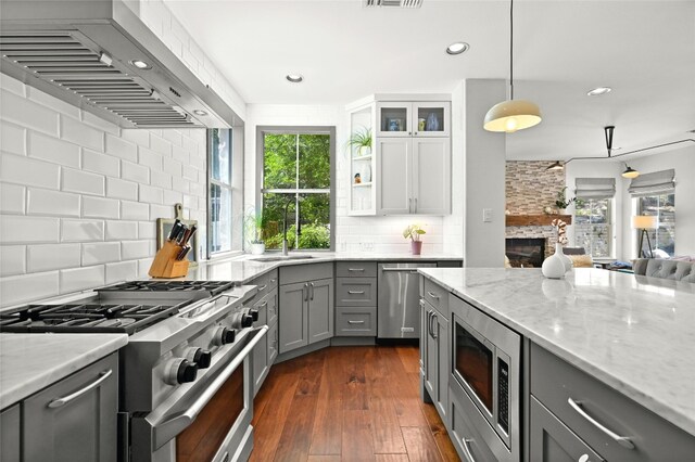4332 Canoas Dr, Austin, TX 78730 - kitchen with gray cabinetry, stainless steel appliances, extractor fan, light stone counters, and decorative backsplash