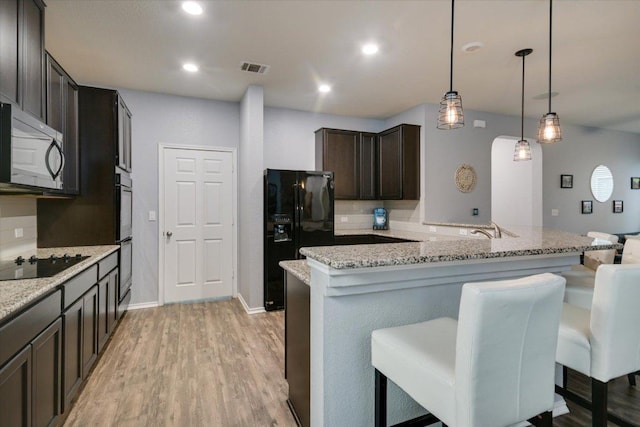 806 Thrasher Glade Dr, Pflugerville, TX 78660 - kitchen featuring black appliances, dark brown cabinets, a breakfast bar area, light wood-style flooring, and light stone counters