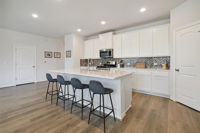 3003 Salvidar Bnd, Austin, TX 78728 - kitchen featuring stainless steel appliances, wood finished floors, a kitchen island with sink, tasteful backsplash, and a breakfast bar area