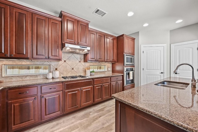 4024 Camacho St, Austin, TX 78723 - kitchen with appliances with stainless steel finishes, stone counters, under cabinet range hood, light wood finished floors, and backsplash
