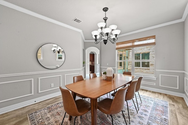 4024 Camacho St, Austin, TX 78723 - dining area featuring arched walkways, a chandelier, light wood-style flooring, crown molding, and a wainscoted wall