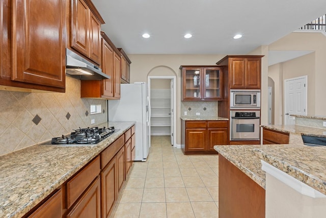 829 Zappa Dr, Cedar Park, TX 78613 - kitchen with stainless steel appliances, under cabinet range hood, light tile patterned floors, decorative backsplash, and arched walkways