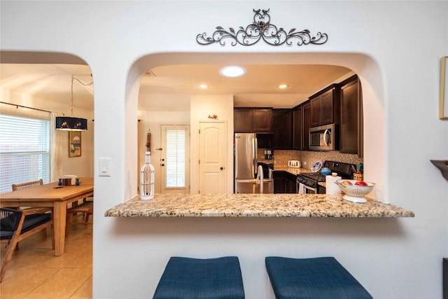 13920 Marathon Rd, Austin, TX 78717 - kitchen featuring appliances with stainless steel finishes, dark brown cabinets, arched walkways, light stone counters, and a breakfast bar