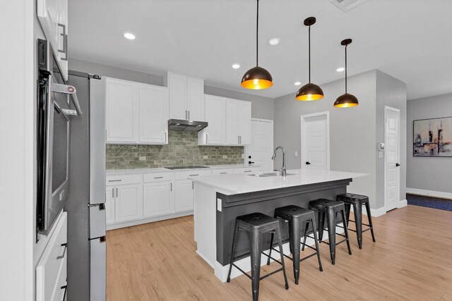 800 Sand Hill Branch Dr Unit 38, Austin, TX 78748 - kitchen featuring under cabinet range hood, light wood finished floors, tasteful backsplash, white cabinetry, and a kitchen bar