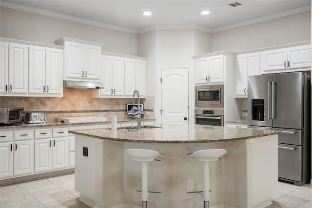 2508 Outlook Ridge Loop, Leander, TX 78641 - kitchen with appliances with stainless steel finishes, under cabinet range hood, a center island with sink, light stone countertops, and decorative backsplash