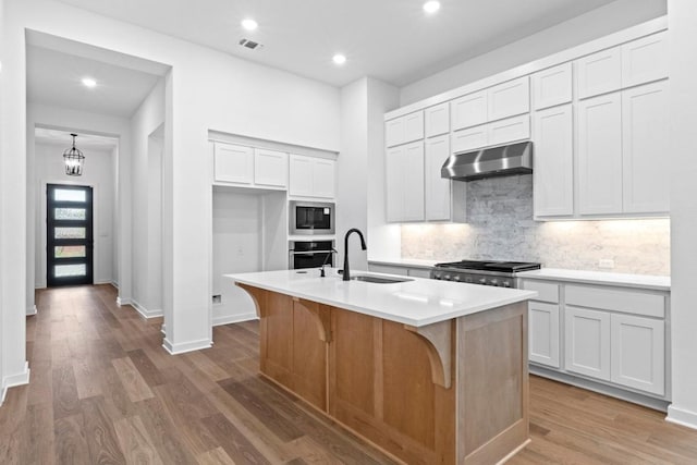 2113 Tobiano Trce, Georgetown, TX 78633 - kitchen featuring exhaust hood, built in microwave, backsplash, a kitchen island with sink, and wood finished floors