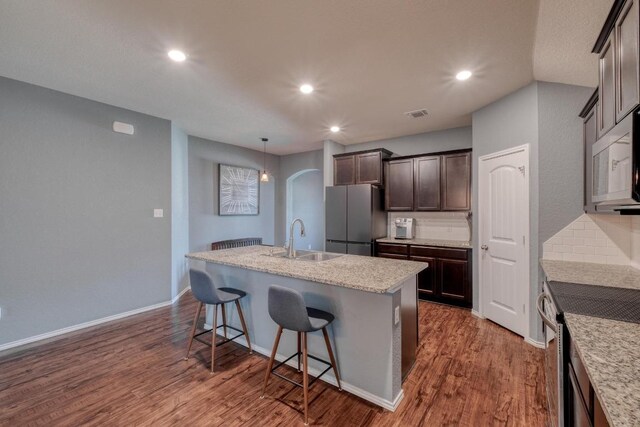 125 Lillian Dr, Taylor, TX 76574 - kitchen featuring appliances with stainless steel finishes, a center island with sink, dark wood-style flooring, arched walkways, and dark brown cabinets
