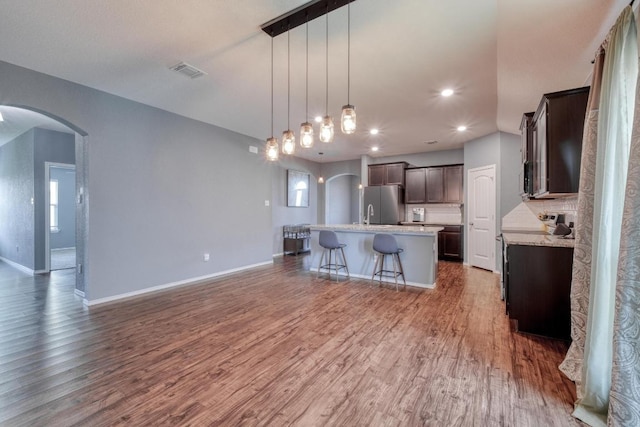 125 Lillian Dr, Taylor, TX 76574 - kitchen featuring arched walkways, freestanding refrigerator, dark brown cabinetry, wood finished floors, and recessed lighting