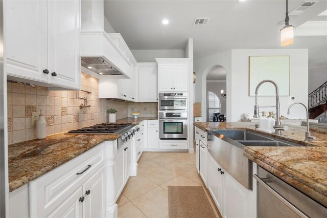 107 Bella Strada Cv, Lakeway, TX 78734 - kitchen with custom range hood, appliances with stainless steel finishes, arched walkways, tasteful backsplash, and light tile patterned floors