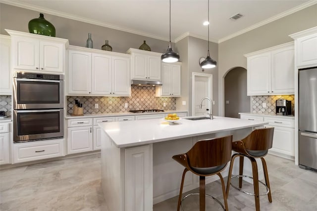 106 Packsaddle Dr, Bastrop, TX 78602 - kitchen featuring stainless steel appliances, decorative backsplash, white cabinetry, a kitchen island with sink, and crown molding