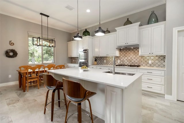 106 Packsaddle Dr, Bastrop, TX 78602 - kitchen with under cabinet range hood, decorative backsplash, a center island with sink, white cabinets, and ornamental molding