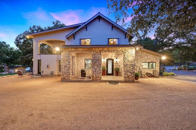 14305 Geronimo St, Leander, TX 78641 - back of house at dusk featuring stone siding, covered porch, and stucco siding