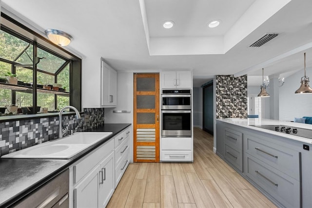 6110 Gardenridge Holw, Austin, TX 78750 - kitchen featuring a tray ceiling, stainless steel double oven, tasteful backsplash, white cabinetry, and light wood-style flooring