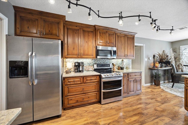 515 Wesley Ridge Dr, Spicewood, TX 78669 - kitchen featuring stainless steel appliances, backsplash, light wood-style floors, brown cabinets, and light stone countertops