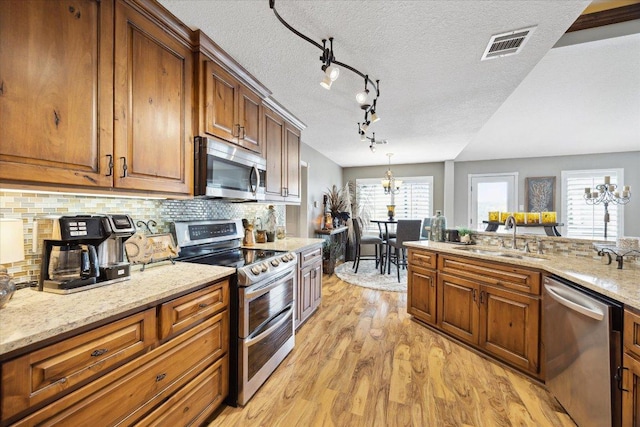 515 Wesley Ridge Dr, Spicewood, TX 78669 - kitchen with stainless steel appliances, light wood-style flooring, a chandelier, decorative backsplash, and a textured ceiling