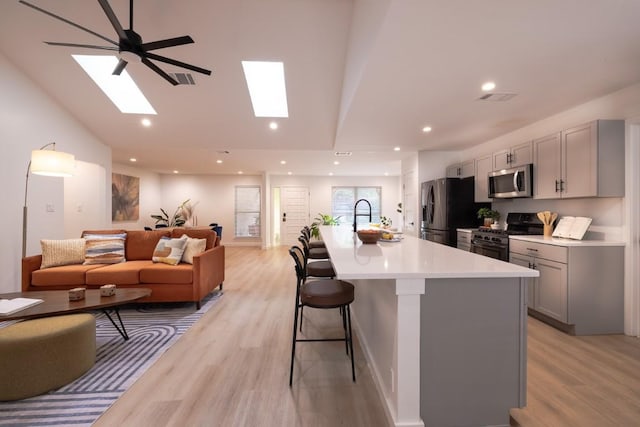 2306 Monarch Dr, Austin, TX 78748 - kitchen with stainless steel appliances, gray cabinetry, open floor plan, a kitchen breakfast bar, and light wood-style flooring