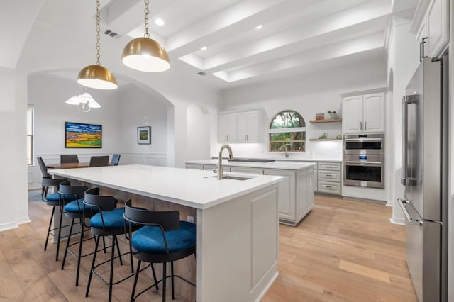 1006 Foothills Dr, Dripping Springs, TX 78620 - kitchen with appliances with stainless steel finishes, a kitchen island with sink, arched walkways, light wood finished floors, and a raised ceiling
