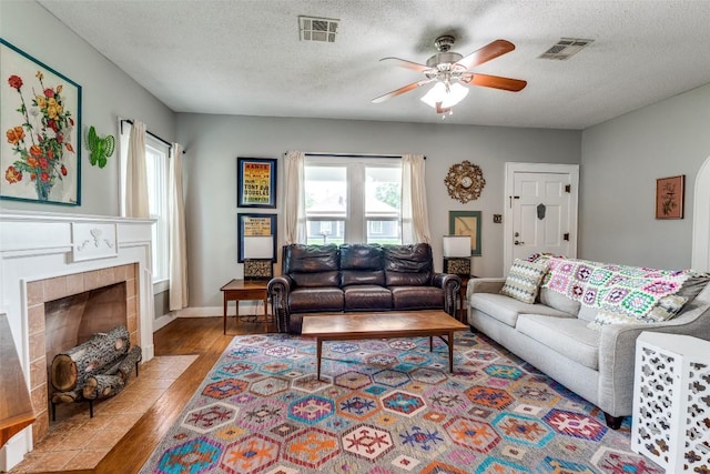 1106 S 11th St, Temple, TX 76504 - living area featuring wood finished floors, a ceiling fan, healthy amount of natural light, a tiled fireplace, and a textured ceiling