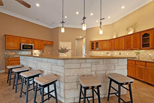 1806 Carey Ave, Taylor, TX 76574 - kitchen featuring stainless steel microwave, brown cabinets, light tile patterned flooring, decorative backsplash, and crown molding