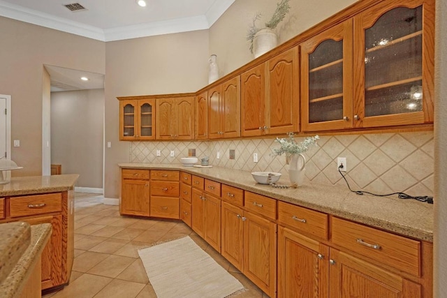 1806 Carey Ave, Taylor, TX 76574 - kitchen with tasteful backsplash, light stone countertops, brown cabinetry, ornamental molding, and glass insert cabinets