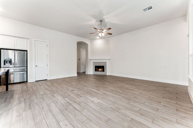 2935 Mckinnie Park, Bulverde, TX 78163 - unfurnished living room featuring ceiling fan, light wood finished floors, arched walkways, and a warm lit fireplace
