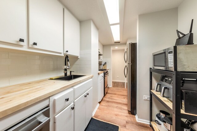 1212 Guadalupe St Unit 301, Austin, TX 78701 - kitchen with stainless steel appliances, light wood-type flooring, white cabinetry, and decorative backsplash