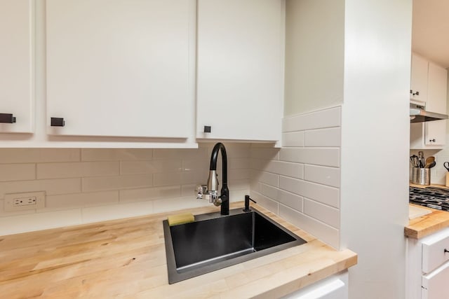 1212 Guadalupe St Unit 301, Austin, TX 78701 - kitchen with butcher block countertops, white cabinets, tasteful backsplash, and under cabinet range hood