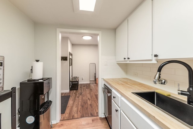 1212 Guadalupe St Unit 301, Austin, TX 78701 - kitchen with light wood-style flooring, white cabinets, decorative backsplash, stainless steel dishwasher, and butcher block counters
