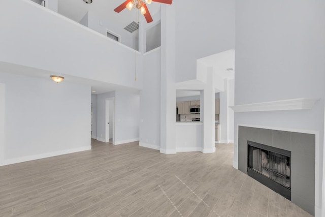 131 Martin Crossing Dr, Cedar Creek, TX 78612 - unfurnished living room featuring a ceiling fan, a towering ceiling, a fireplace, and light wood-style floors