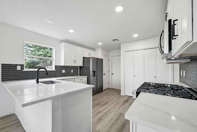 1105 Madrone Trl, Leander, TX 78641 - kitchen featuring stainless steel appliances, tasteful backsplash, white cabinetry, a peninsula, and light wood finished floors