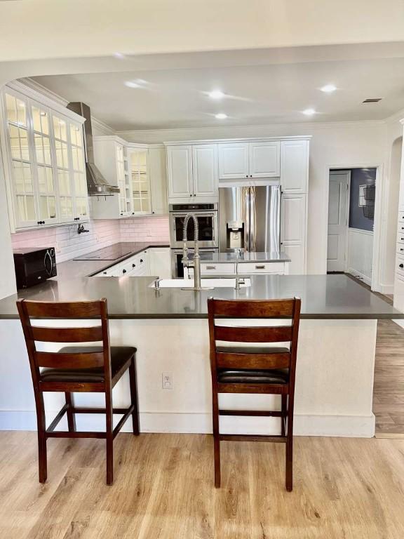 2118 Howell Mountain Dr, Cedar Park, TX 78613 - kitchen featuring black appliances, wall chimney range hood, dark countertops, light wood-style flooring, and glass insert cabinets