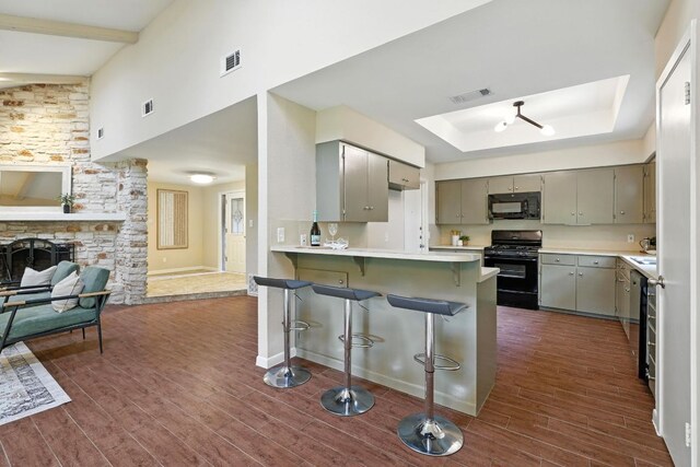 11915 River Oaks Trl, Austin, TX 78753 - kitchen featuring black appliances, gray cabinetry, a peninsula, dark wood-style flooring, and a breakfast bar