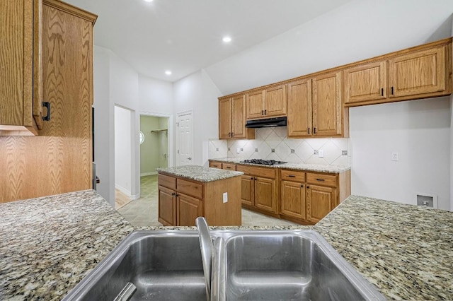 501 Flamingo Blvd, Lakeway, TX 78734 - kitchen with under cabinet range hood, decorative backsplash, gas stovetop, brown cabinets, and light stone countertops