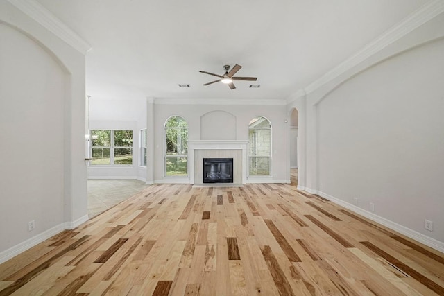501 Flamingo Blvd, Lakeway, TX 78734 - unfurnished living room featuring light wood-type flooring, ceiling fan, a tiled fireplace, crown molding, and arched walkways