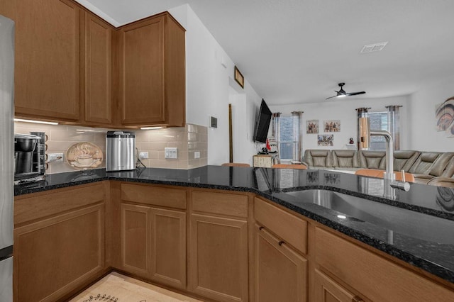 4909 Teverola Dr, Round Rock, TX 78665 - kitchen featuring open floor plan, ceiling fan, dark stone countertops, decorative backsplash, and brown cabinetry