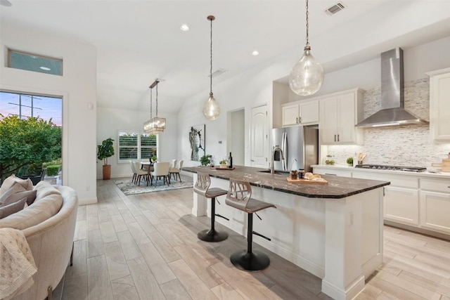 405 Maialina Cv, Lakeway, TX 78738 - kitchen with wall chimney range hood, stainless steel appliances, backsplash, light wood finished floors, and a kitchen breakfast bar