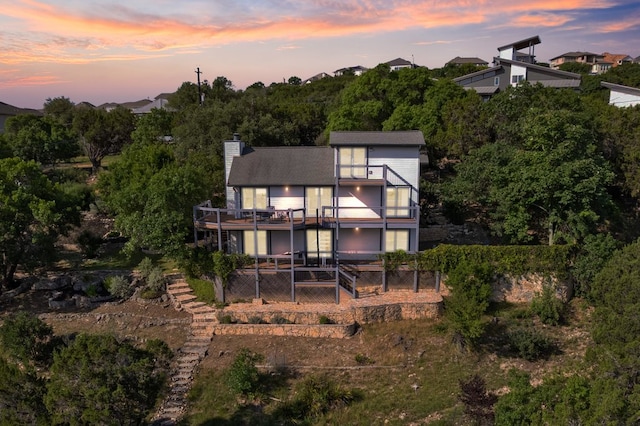 19426 Fisher Ln, Spicewood, TX 78669 - back of house at dusk with a balcony, a fenced backyard, a chimney, and a patio
