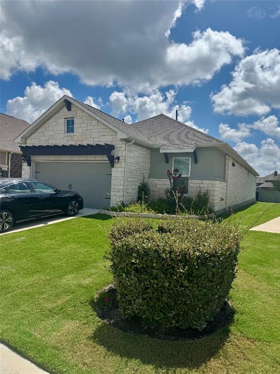 821 Faith Dr, Liberty Hill, TX 78642 - view of side of home featuring an attached garage, a lawn, roof with shingles, driveway, and stone siding